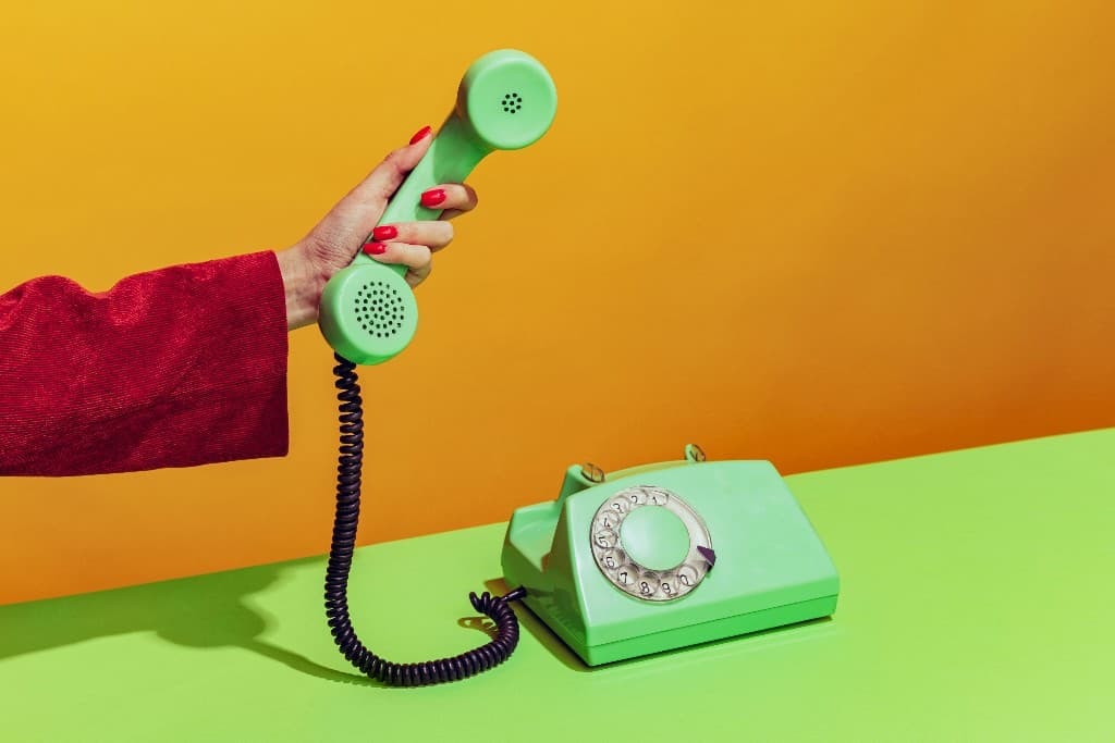 Hand holding a green rotary telephone receiver above the base